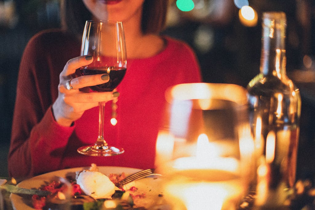 A woman enjoying red wine at a romantic candlelit dinner, perfect for celebrations.