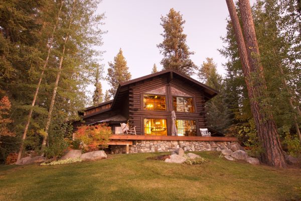 Cozy log cabin surrounded by tall trees at sunset, with warm glowing lights
