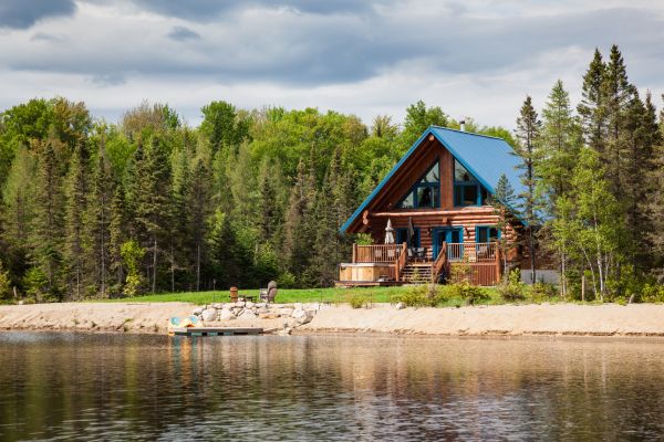 Lakefront log cabin with blue roof surrounded by pine trees and water views.