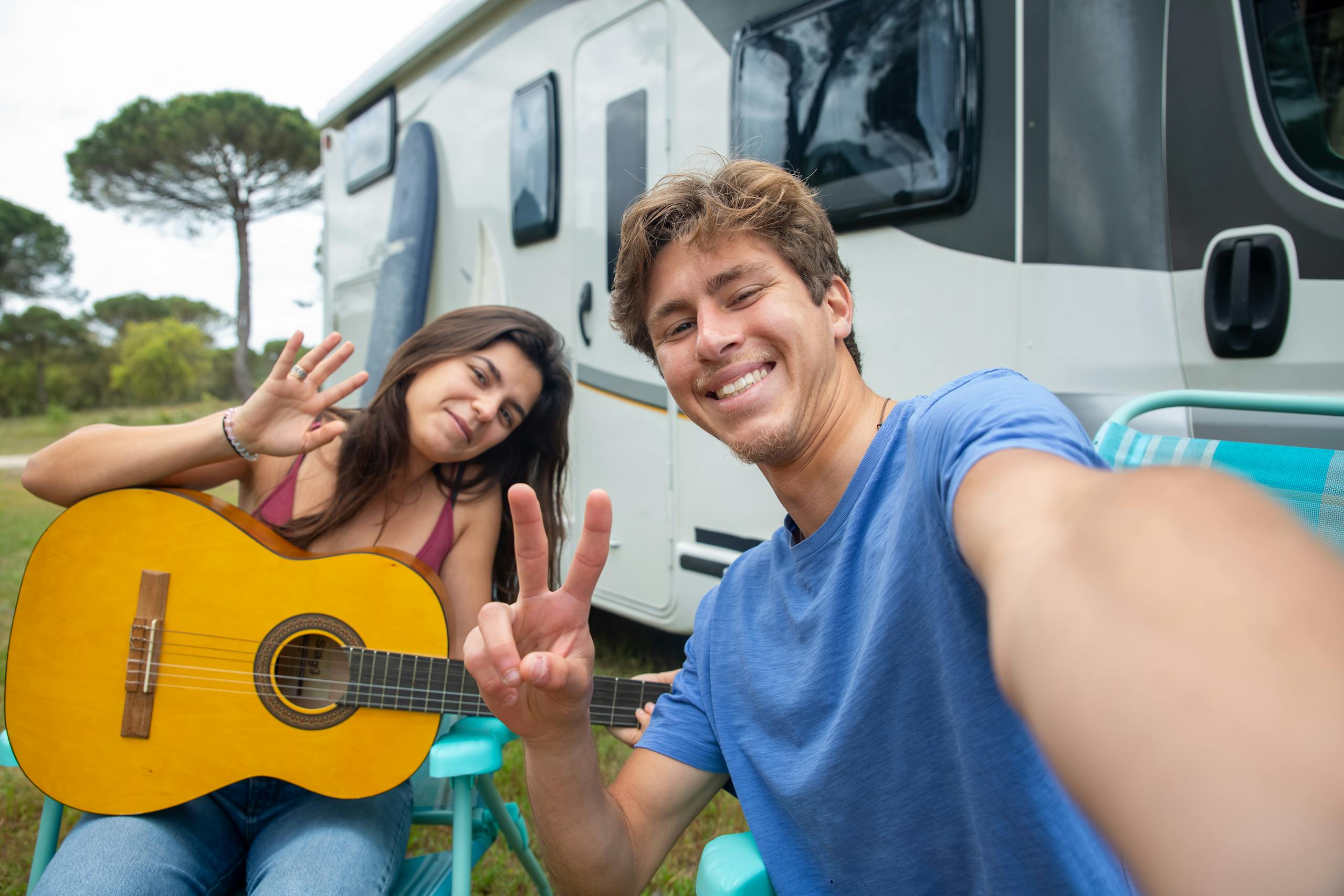 A happy couple sitting outdoors by a camper, enjoying music and taking a selfie in Portugal.